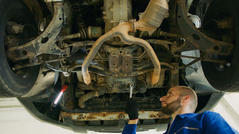 Professional mechanic examining vehicle undercarriage for repair in a garage.